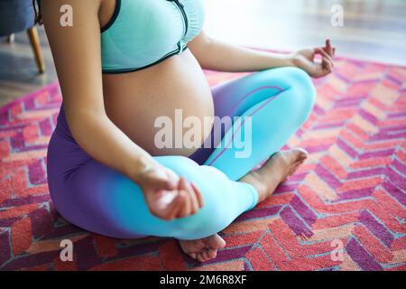 Nahaufnahme einer schwangeren Sportlerin, die Yoga praktiziert, in Lotus-Pose meditiert Stockfoto