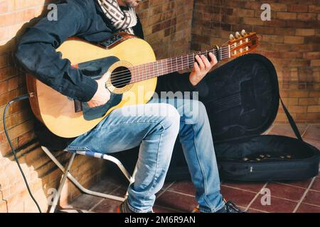 Ein männlicher Streuner, der spanische Akustikgitarre spielt, mit einem kleinen Verstärker auf der Straße Stockfoto