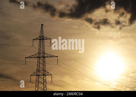 Silhouette eines Hochspannungsturms mit elektrischen Drähten auf dem Hintergrund des Sonnenuntergangs und dunkler Wolken. Stromübertragungsleitungen, Stromversorgung Stockfoto