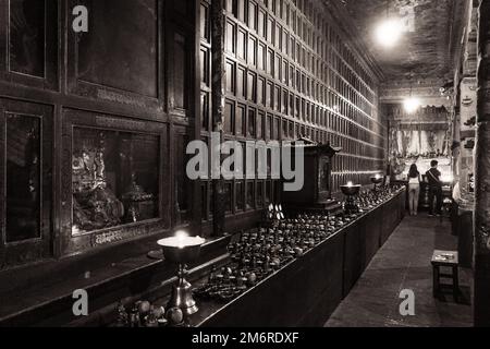 Kerzen und Opfergaben an einer dekorierten Wand aus Schränken und Figuren, Kumbum Kloster, Xining, China Stockfoto