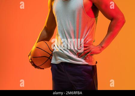 Bild des Mittelabschnitts des biracial Basketballspielers mit Basketball auf orangefarbenem bis gelbem Hintergrund Stockfoto