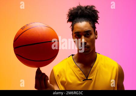 Bild eines biracial Basketballspielers Spinning Basketball auf rosa bis orange Hintergrund Stockfoto