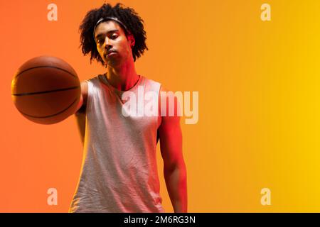 Bild von biracial Basketballspieler mit Basketball auf orange bis gelb Hintergrund Stockfoto