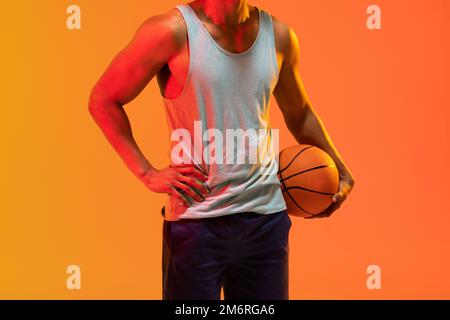 Bild des Mittelabschnitts des biracial Basketballspielers mit Basketball auf orangefarbenem bis gelbem Hintergrund Stockfoto