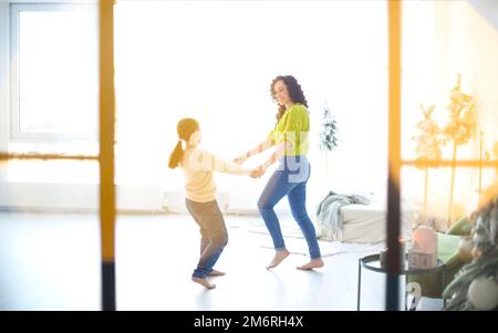 Glückliche Familie zu Hause. Kleine Tochter tanzt mit lächelnder positiver mutter in einem hellen, sonnigen Raum Stockfoto