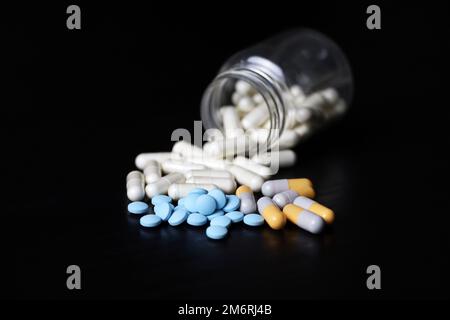 Pillen auf einem schwarzen Holztisch, Variation der Medikamente in Kapseln, die aus einer Flasche verstreut sind. Hintergrund für Pharmazie, Antibiotika, Vitamine Stockfoto