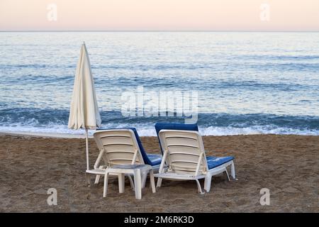 Leere weiße und blaue Sitze am Strand in der Nähe des Meeres am frühen Morgen Stockfoto