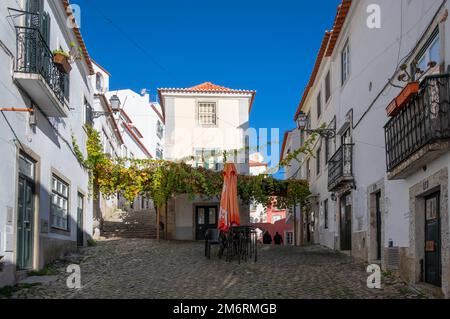 Wunderschöne, enge Kopfsteinpflasterstraßen zusammen mit traditionellen bunten Häusern, Cafés und Restaurants im Alfama-Viertel, Lissabon, Portugal. Stockfoto