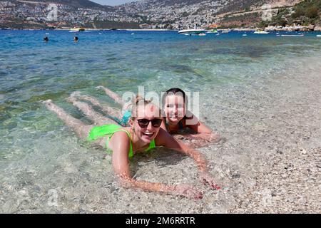 Zwei lächelnde junge Frauen (Modell veröffentlicht) genießen das Meerwasser im Kalkan Beach Club in Kalkan, Türkei. Juli 2022 Stockfoto