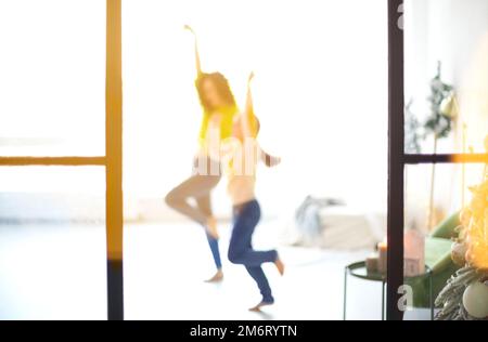 Glückliche Familienmutter und kleine Tochter, die Händchen hält und in einem hellen, sonnigen Raum tanzt Stockfoto