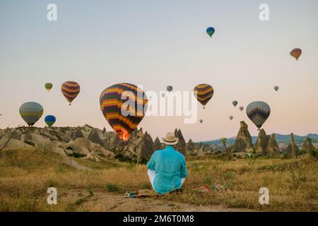 Junge Männer beobachten Heißluftballons während des Sonnenaufgangs in Kappadokien, Türkei, Kapadokya Goreme Stockfoto