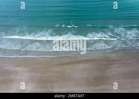 Blick von oben auf die Drohne auf das türkisfarbene Meer und die weißen Wellen, die an einem goldenen Sandstrand brechen Stockfoto