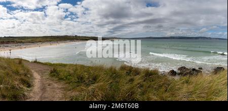 Panorama-Landschaft eines sandigen Fußwegs, der durch Sanddünen zum Gwithian Beach führt, mit vielen Beachgängern und Surfern im Wasser Stockfoto