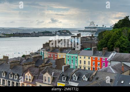 Farbenfrohe Häuser in der Innenstadt von Cobh mit einem riesigen Kreuzfahrtschiff im Hafen von Cork Stockfoto