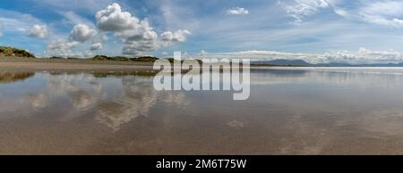 Friedliche Panoramalandschaft eines leeren goldenen Sandstrands mit Reflexionen des Himmels und der Sanddünen Stockfoto