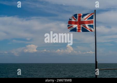 Zerrissene und zerrissene Union-Jack-Flagge in einem steifen Wind mit blauem Meer und Himmel dahinter Stockfoto