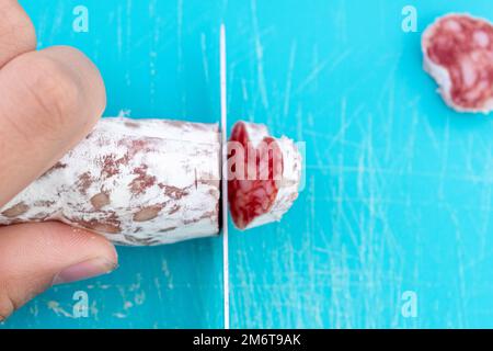 Eine Draufsicht der Hand, die Fuet mit dem Messer zerkleinert Stockfoto