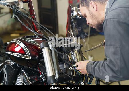 Ein Elektriker lötet elektrische Drähte an elektrische Geräte in einem Motorrad. Nahaufnahme. Transportkonzept Stockfoto