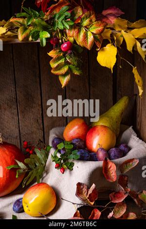Verschiedene Früchte in einer Holzkiste mit Herbstblättern Stockfoto
