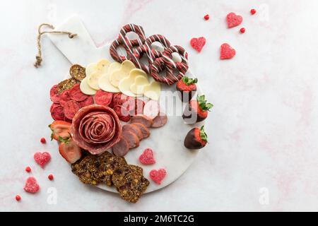 Ein Arrangement mit Wurstwaren am Valentinstag auf einer weißen Marmorplatte. Stockfoto