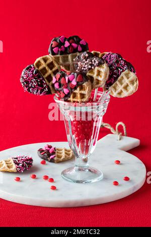Ein mit Zimt gefülltes Dessertglas mit dekorierten Valentinstag-Waffelpops. Stockfoto