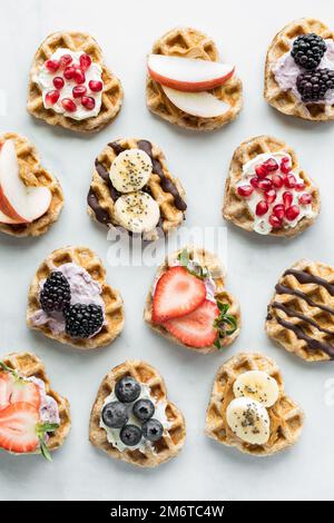 Herzförmige Mini-Waffeln mit verschiedenen Belägen in Reihen. Stockfoto