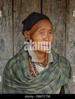 Mon, Nagaland, Indien - 03 03 2009 : Porträt einer alten ethnischen Naga-Frau mit grünem Karomuster, traditioneller Halskette und schwarzem Schal auf Holzhintergrund Stockfoto