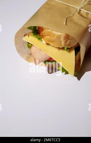 Sandwich mit Käse und Schinken, in Papier eingewickelt auf weißem Hintergrund mit Kopierbereich Stockfoto