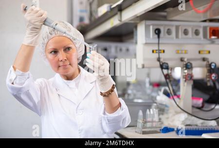 Fokussierte Chemikerin Pipettiert blaues Reagenz in Lösung im Reagenzglas während Experimenten im Forschungszentrum Stockfoto