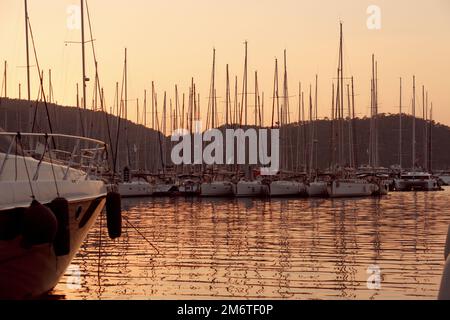 Festgemachte Yachten. Yachthafen, Hafen. Reflexion von Bootsmasten im Meerwasser bei Sonnenuntergang Stockfoto