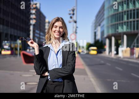 Porträt einer erfolgreichen jungen geschäftsführerin, Geschäftsfrau in schwarzem Anzug, auf einer sonnigen Straße stehend und lächelnd Stockfoto