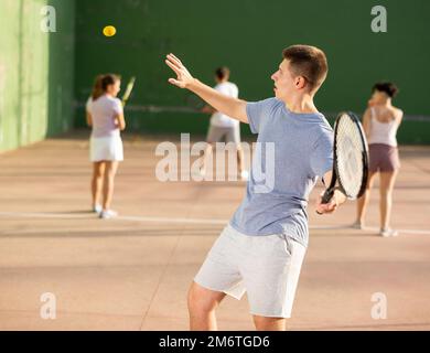 Junger männlicher Pelotaspieler trifft Ball mit Schläger Stockfoto