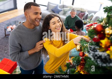 Bild eines glücklichen, vielfältigen Paares, das zu Hause weihnachten feiert und den Baum dekoriert Stockfoto
