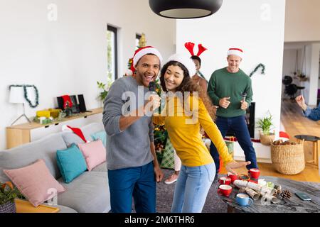 Bild eines glücklichen, vielfältigen Paares, das mit Freunden zu Hause Karaoke singt Stockfoto