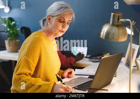 Ein vielseitiges Senior-Paar, das am Tisch sitzt und arbeitet Stockfoto