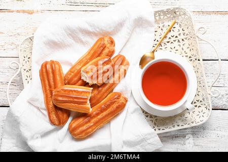 Tablett mit leckeren Eclairs und einer Tasse Tee auf hellem Holzhintergrund Stockfoto