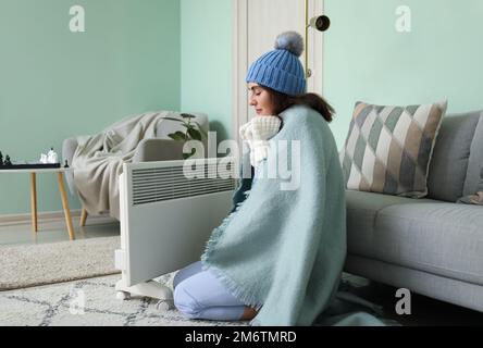 Gefrorene junge Frau mit Karomuster in der Nähe der Heizung zu Hause Stockfoto