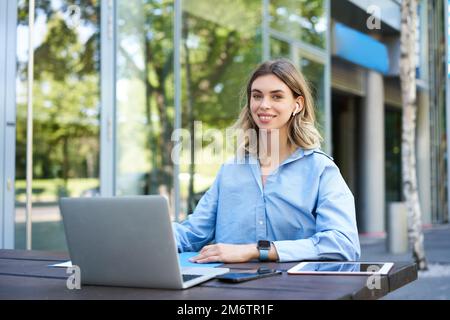 Portrait of young beautiful working woman, works on remote with laptop. Student takes notes during online video conference, sitt Stockfoto