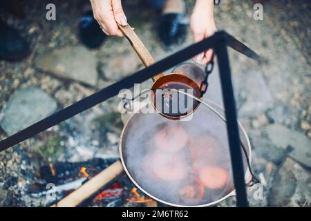 Von oben traditioneller Glühwein mit Orangenscheiben, die in Töpfen über brennenden Stämmen zubereitet werden Stockfoto