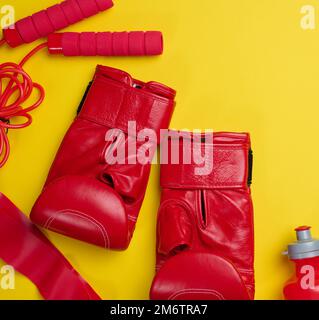 Boxhandschuhe aus rotem Leder, Wasserflasche. Sportausrüstung auf gelbem Hintergrund Stockfoto