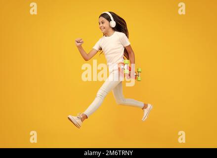 Teen girl 12, 13, 14 Jahre alt mit Skateboard über Studio Hintergrund. Springt und lauft. Cooler moderner Teenager in stilvoller Kleidung. Teenager-Lifestyle Stockfoto