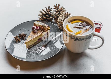 Wintercafé-Set. Leckerer Wintertee mit Nelken und Orangenscheiben serviert mit Blaubeerkäsekuchen. Speicherplatz kopieren. Hochwertiges Foto Stockfoto