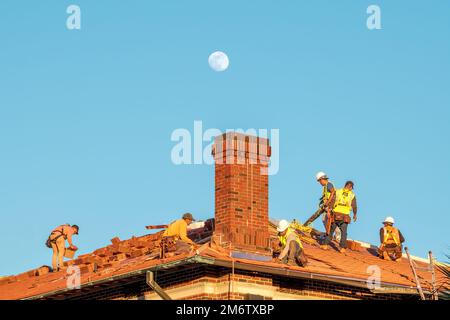 New Orleans, LA, USA - 4. JANUAR 2023: Arbeiter ersetzen Dachziegel auf einem Dach mit dem Mond im Hintergrund Stockfoto