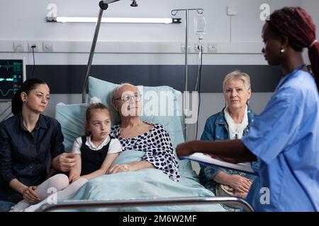 Chirurg, der notwendige Papiere ausfüllt, um kranken älteren Mann für einen medizinischen Eingriff im Operationssaal aufzunehmen. Chronisch kranker Großvater, der von einem afroamerikanischen Arzt betreut wird. Stockfoto
