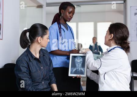 Medizinisches Personal weibliche Mitglieder, die kranke junge Frau in der Krankenhauslobby betreuen. afroamerikanischer Krankenpfleger als Assistenzarzt in der Sprechstunde der Medizinischen Klinik. Arzt, der Testergebnisse liefert. Stockfoto