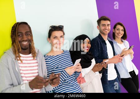 Verschiedene Jugendliche nutzen mobile Geräte, während sie vor einem farbenfrohen Hintergrund für ein Studiofoto posieren Stockfoto