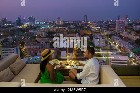 Ein paar Männer und Frauen essen während des Sonnenuntergangs in einem Dachrestaurant mit Blick auf die Stadt zu Abend Stockfoto