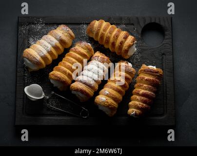 Gebackene Tubuli gefüllt mit Schlageier weißer Creme auf einem schwarzen Küchenbrett aus Holz, Draufsicht Stockfoto