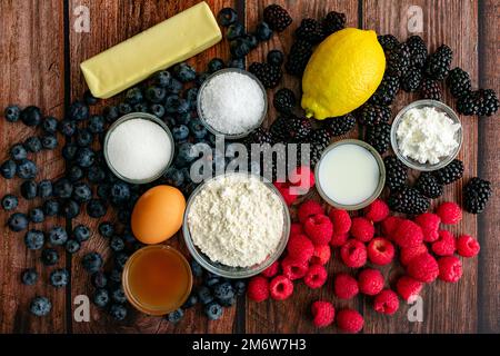 Mixed Berry Galette Ingredients on a Wood Table: Rohe Zutaten einschließlich frischer Beeren, die für eine rustikale Desserttart verwendet werden Stockfoto