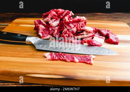 Dünn geschnittenes Ribeye Steak auf einem Holzschneidebrett mit einem Messer: Dünn geschnittene Rinderstreifen mit einem santoku-Messer auf einem Holzschneidebrett Stockfoto